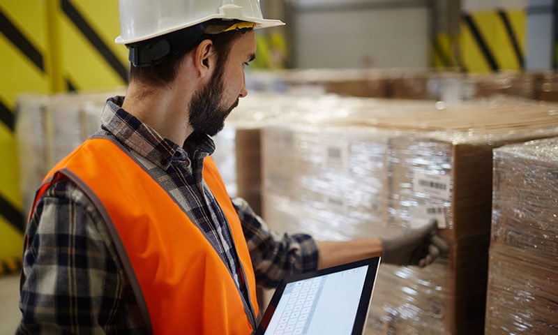 Logisticien dans l’entrepôt contrôlant les expéditions des commandes avec un logiciel logistique